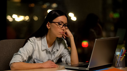 Young woman bored working on laptop in office, lacking motivation, unloved job