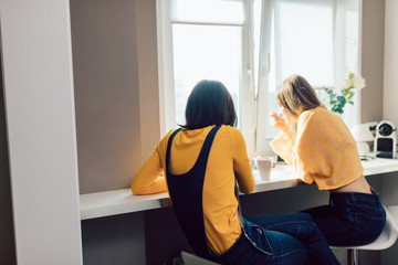 Two sisters in stylish casual clothes drinking tea, talking in the morning. back view close up photo. conversation. two women having a chat, friendship concept