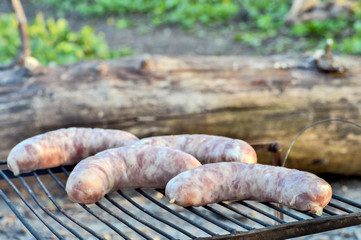 Raw sausages laid out on the grill for cooking on the coals