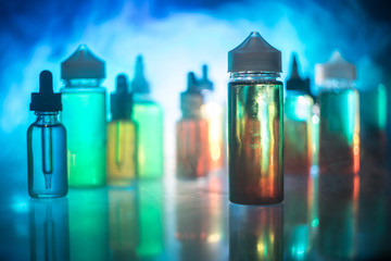Vape concept. Smoke clouds and vape liquid bottles on dark background. Light effects. Useful as...