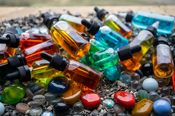 Vape concept. Beautiful colorful vape liquid glass bottles outdoor on stones. Useful as background...