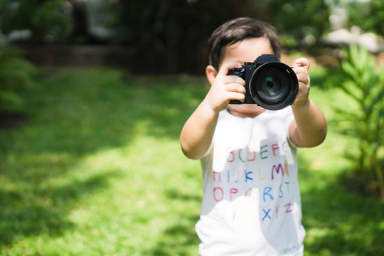 Young asian boy taking photo by camera in park area at home