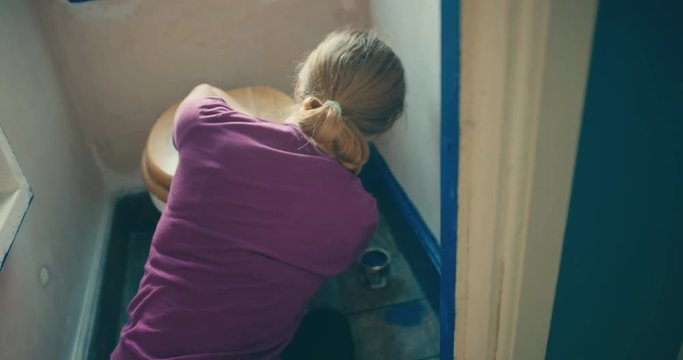 Young woman painting skirting board in small toilet