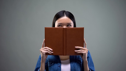 Woman making plans and thinking over business strategy hiding behind notebook