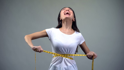 Screaming woman tightening measuring tape, strong desire to be slim, problem