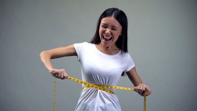 Young woman tightening measuring tape, torturing herself with diet, bulimia