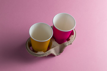 two violet and yellow empty paper cups isolated on pink background. close up photo.recycling paper
