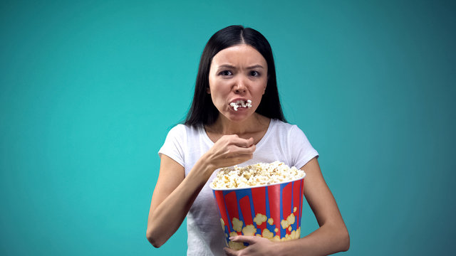 Focused on movie woman devouring popcorn from big paper cup, unhealthy eating