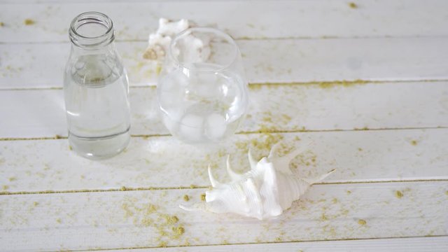 Glass with water and white seashells on wooden table with sand