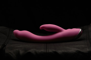 Pink dildo on black skin. Dark background. Artistic lighting.