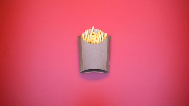 Crispy french fries in carton package on pink background, fast food meal, snack
