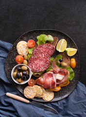 Sandwiches of whole grain bread with ham, bacon, prosciutto, olives and olives with whole grain chips on a black wooden background. Clean food, healthy Breakfast. Top view with copy space