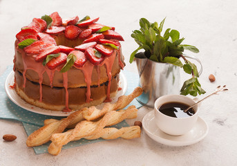 Strawberry cake decorated with mint leaves, cookies and a Cup of coffee on a light background.