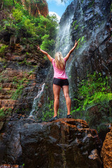 Woman stands on rock in front of cascading waterfall