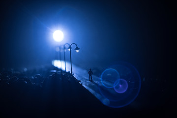 The silhouette of a man in shorts, standing in the middle of the road on a misty night. The glare of the street light against the fog sets a creepy mood. Concept of thieves, rapist and killers roaming