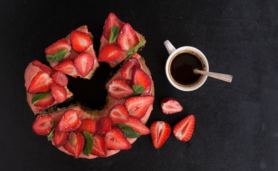 Strawberry pie decorated with mint leaves and a Cup of coffee on a black wooden background. The view from the top. Copy space