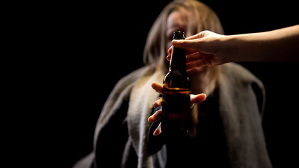 Hand giving beer bottle to alcoholic woman, miserable life, addiction concept