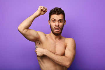 Fototapeta premium crying shirtless man waxing his armpits to depilate hair. close up photo.isolated blue background.