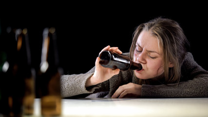 Addict woman lying on table and drinking beer, suffering hangover, hopelessness