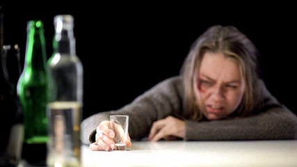 Bruised woman looking with disgust at empty glass, harmful habits, alcoholism