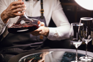 Skilled sommelier holding decanter with red wine. Degustation of wine process in wine boutique,...