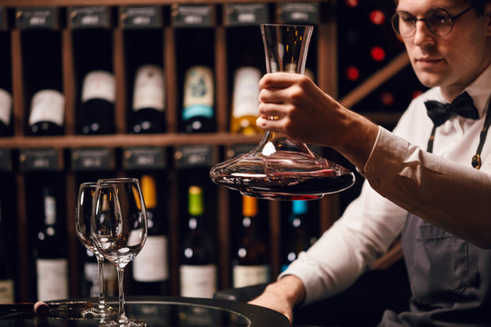 Wine taster or degustator mixing red wine into carafe to make perfect color on background with wine bottles racks in wine house.