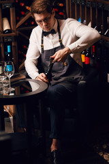 Young handsome sommelier pulling cork out of a bottle using a sommelier knife. Cropped photo of a waiter opening red wine bottle with corscrew in restaurant