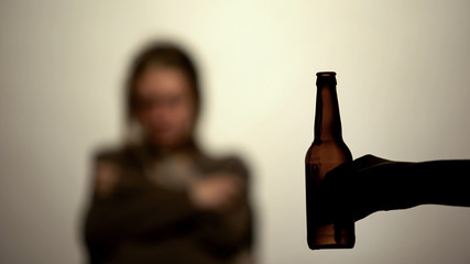 Bottle of beer in hand offering to drink alcohol, addicted woman on background