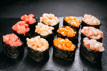 Sushi set gunkan maki with salmon, tuna and prawn served on black stone slate. Delicious traditional Japanese meals, tasty seafood, restaurant menu concept, degustation, banquet, food background