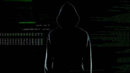Male hacker silhouette in hoodie standing in front of animated computer code