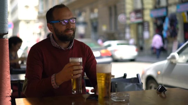 Happy man gets beer frow waiter by the table at city cafe