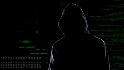 Faceless male hacker in hoodie standing in front of animated computer code