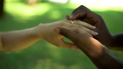 Multiracial marriage, male hand puts golden ring on brides finger, wedding time
