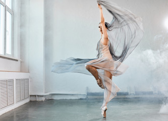 Fototapeta premium Full size portrait of talanted ballet student woman wears grey fluttering scenic dress giving a performance on a final exam in light studio on white smoky background.