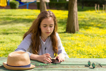 Pretty teenager girl listening to music by mobile cellpfone smartphone at the summer park