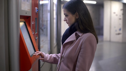 Young female tourist buying tickets in self-service terminal, making payment
