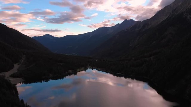 Aerial, rising, drone shot, of a mirroring lake, surrounded by alp mountains and forest, on a sunny evening sunset, at Lago Di Anterselva, in Parco Naturale Vedrette di Ries Aurina, south Tirol, Italy