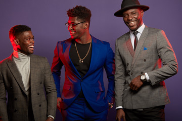 Band of cheerful popular african musicians or singers in fashionable classy wear making poster for musical magazine cover, posing before camera in studio