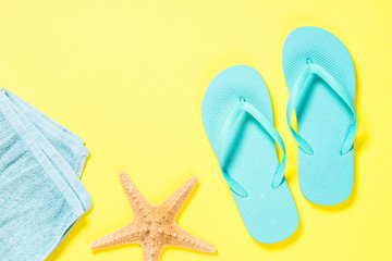 Blue flip flops, sunglasses and starfish on yellow background.