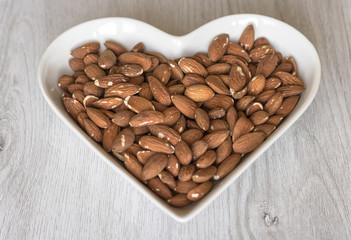 Nuts arranged in heart  on background. Healthy Food image close up almond on the cup plate. Love Texture on white grey table top view mock up