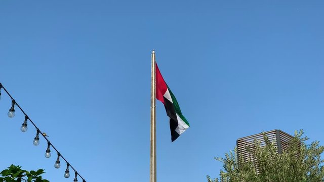 UAE flag waving in Dubai city , national symbol of UAE. blue sky, uae flag perfect for film, news, digital composition