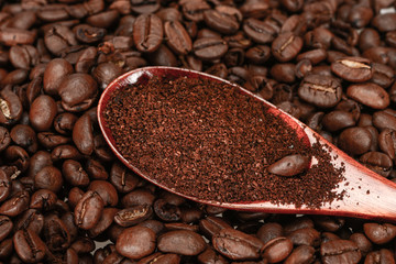 Red bamboo spoon with ground coffee, lies on roasted coffee beans, close-up, isolated on a white background