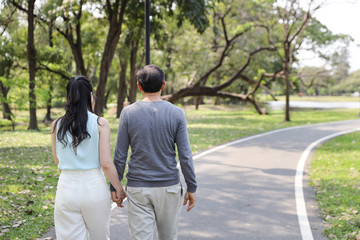 back view asian couple walking and talking in the park with happy face