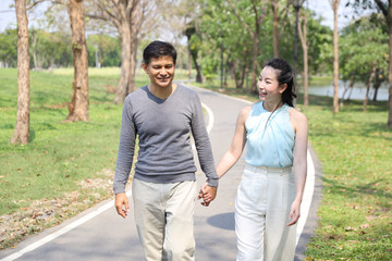 asian couple walking and talking in the park with happy face