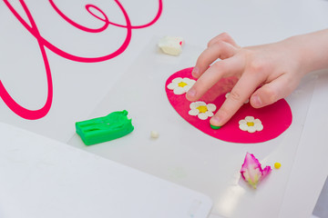 Hands of little girl making spring card with flowers from colorful clay dough (plasticine)
