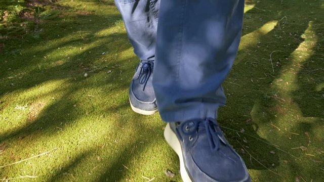 Man wearing blue trousers and blue loafer shoes, walking on green moss through sun and shadows. UHD