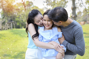 Obraz premium image of happy family, daughter putting her hands on parents cheek with smiling while father and mother kissing during summer time in the park