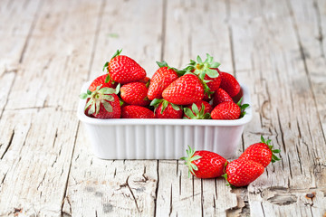 Fresh red strawberries in white bowl and mint leaves on rustic wooden background.