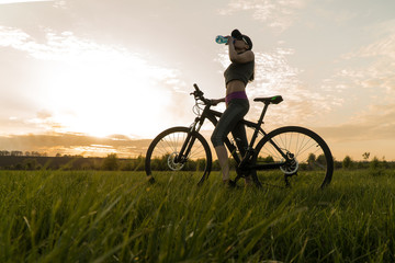 Fototapeta premium drink water during workouts. sports. woman on bike sunset