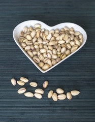 Nuts arranged in heart  on background. Healthy Food image close up pistachios on the cup plate. Love Texture on top view mock up